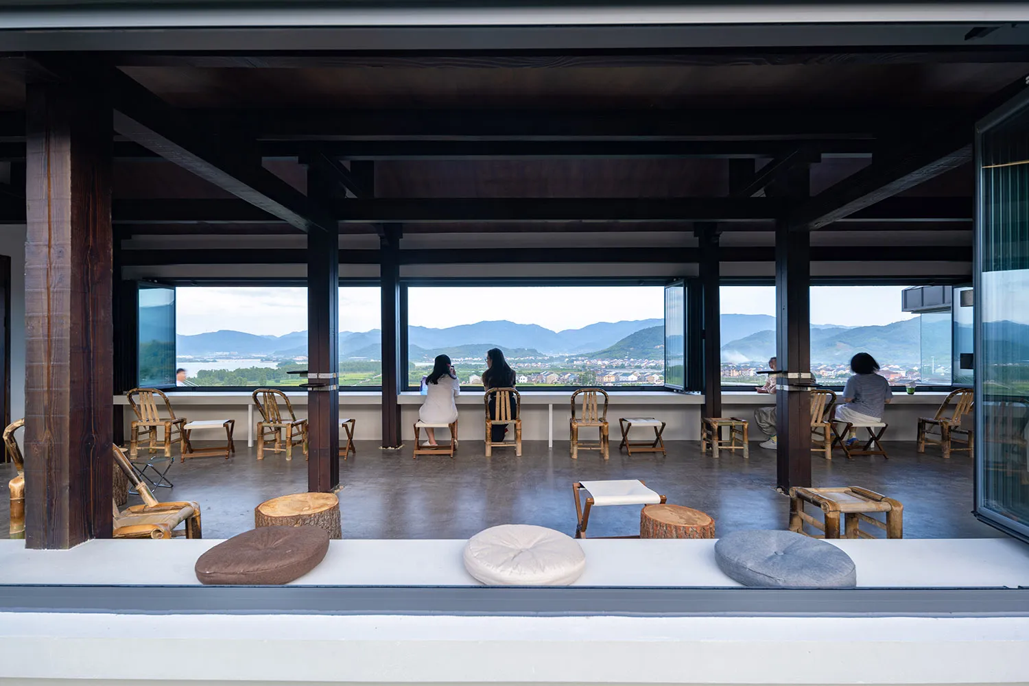 Outdoor dining area with wooden furniture, tables, and chairs, surrounded by a mountain landscape with a relaxed and inviting atmosphere