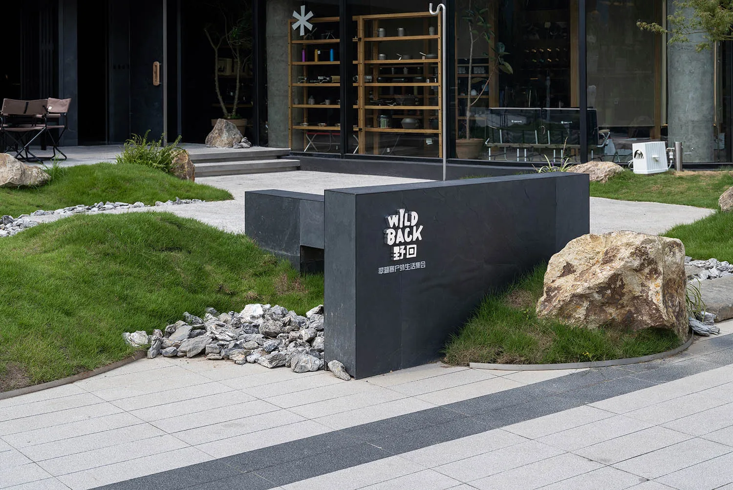 A serene outdoor space with a black stone bench and potted plants surrounding a building