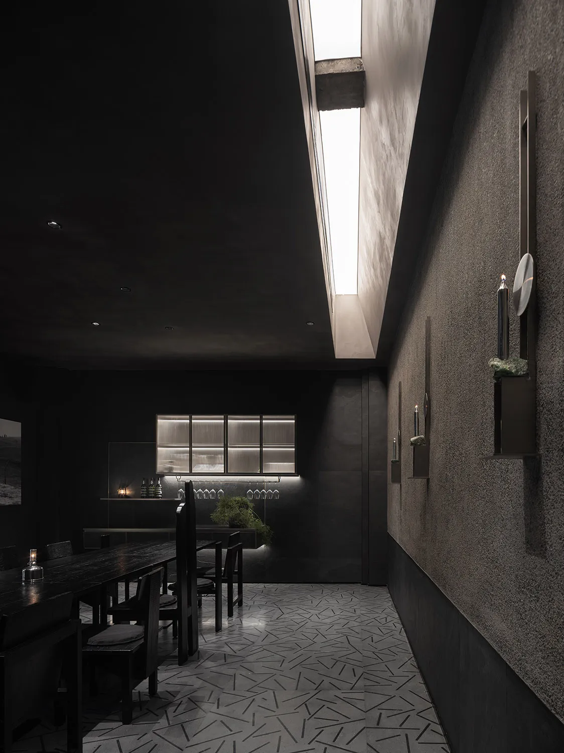Dark restaurant interior with black walls and floors, featuring dining tables and chairs, and scattered bottles
