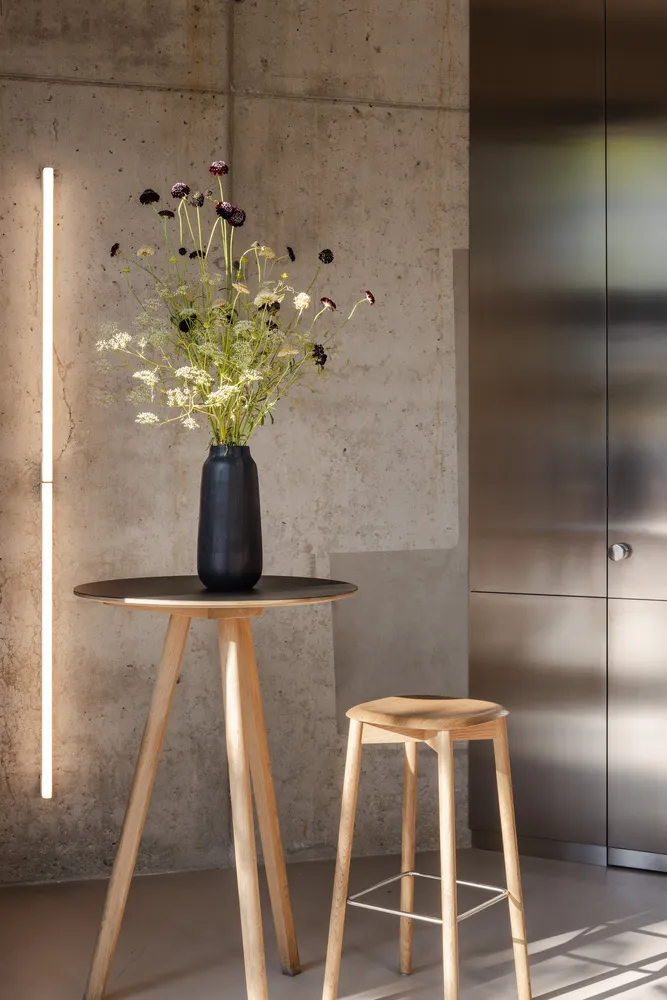 A cozy living space with a wooden table, two chairs, and a black vase filled with flowers, creating a warm and inviting atmosphere