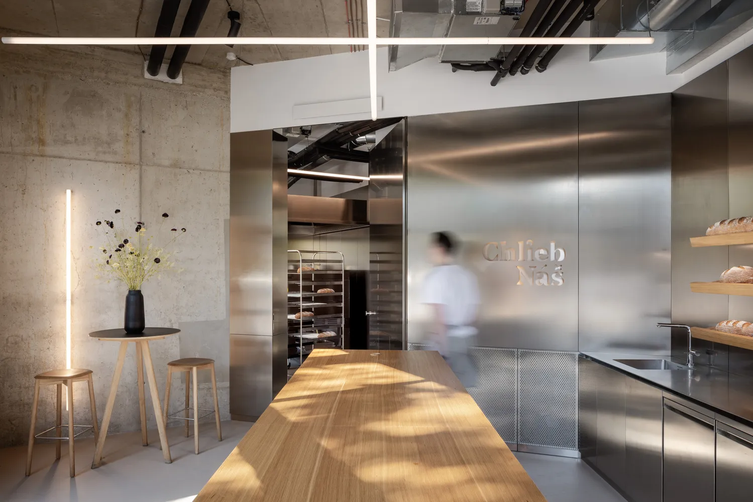 A modern kitchen with a wooden table and two ovens, surrounded by chairs, in a well-lit space with a focus on functionality and aesthetics