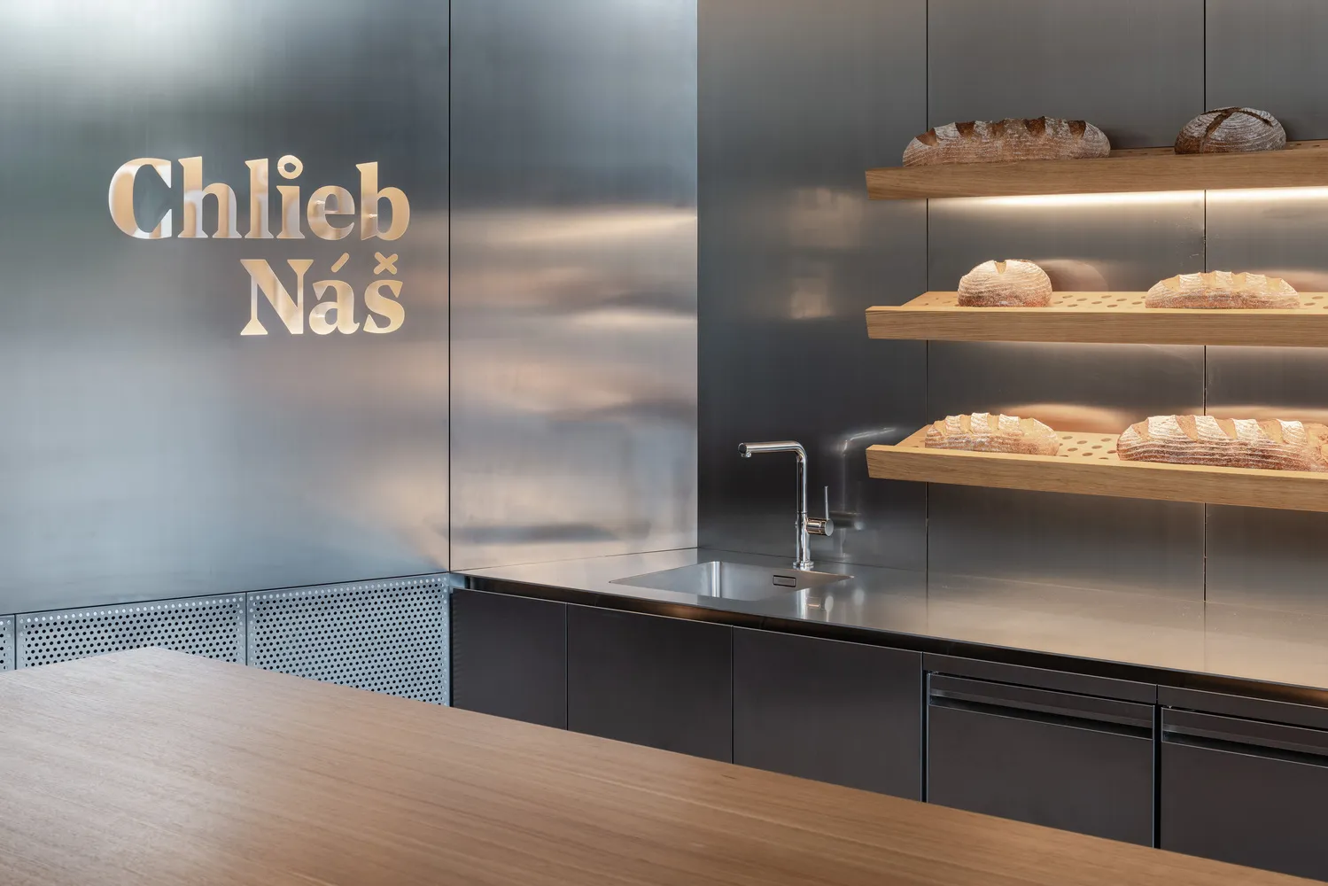 A modern kitchen with two sinks, a countertop, and shelves displaying various types of bread and baked goods, in a clean and organized atmosphere