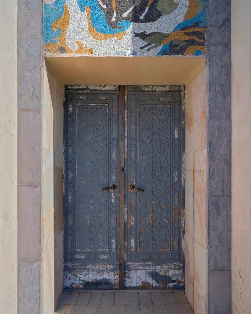 A traditional doorway with a metal frame and stone arch, set in a historic building with a wooden door and rustic appearance