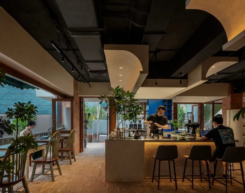 Warm and inviting restaurant interior with a bar area, dining tables, and potted plants, featuring brick walls and a rustic atmosphere