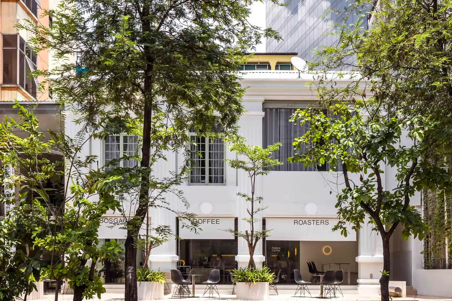 A coffee shop with a white facade, outdoor seating, and dining tables, creating a relaxed atmosphere