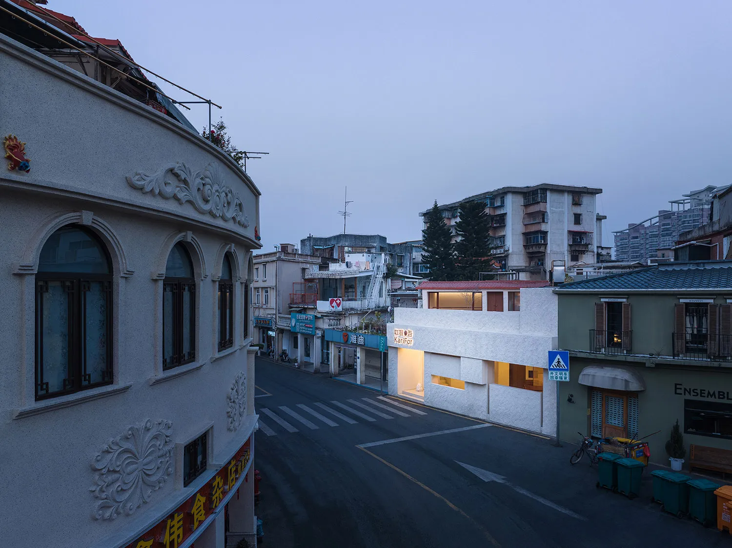 A bustling Asian city street at night with a mix of residential and commercial buildings, featuring people and vehicles, and decorative white buildings with arches