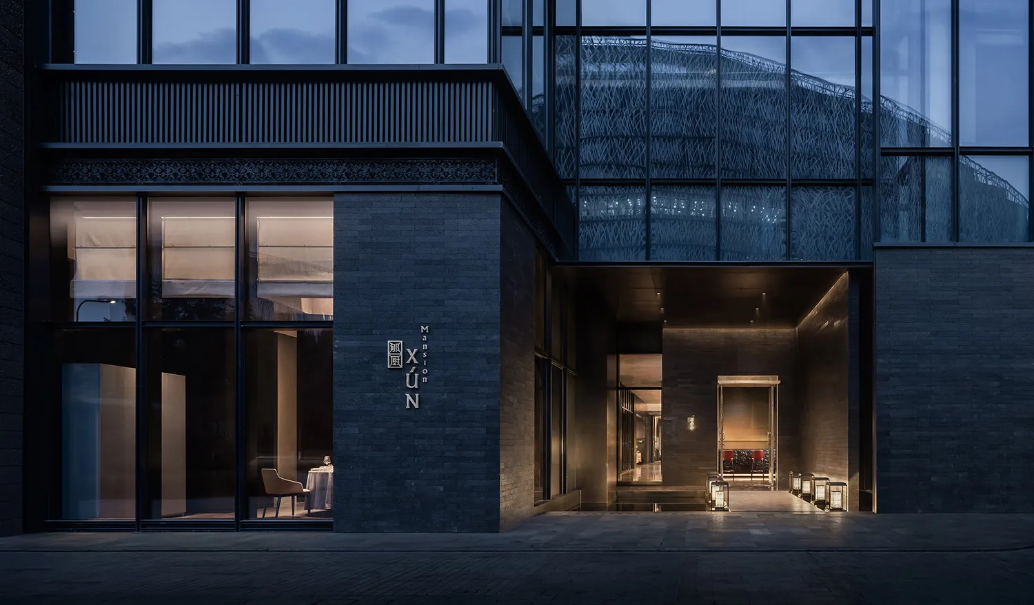 A modern glass building at night with a spacious interior, featuring chairs and dining tables, and a contemporary atmosphere