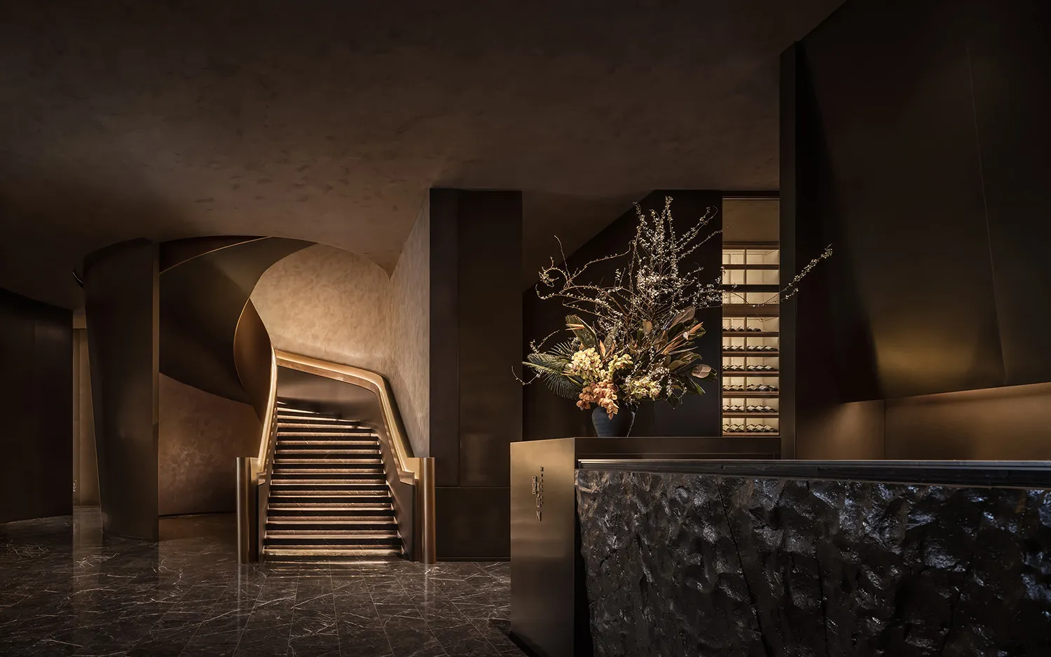 Spiral marble staircase in a luxurious lobby with a large vase on a table, surrounded by high-end design and decoration