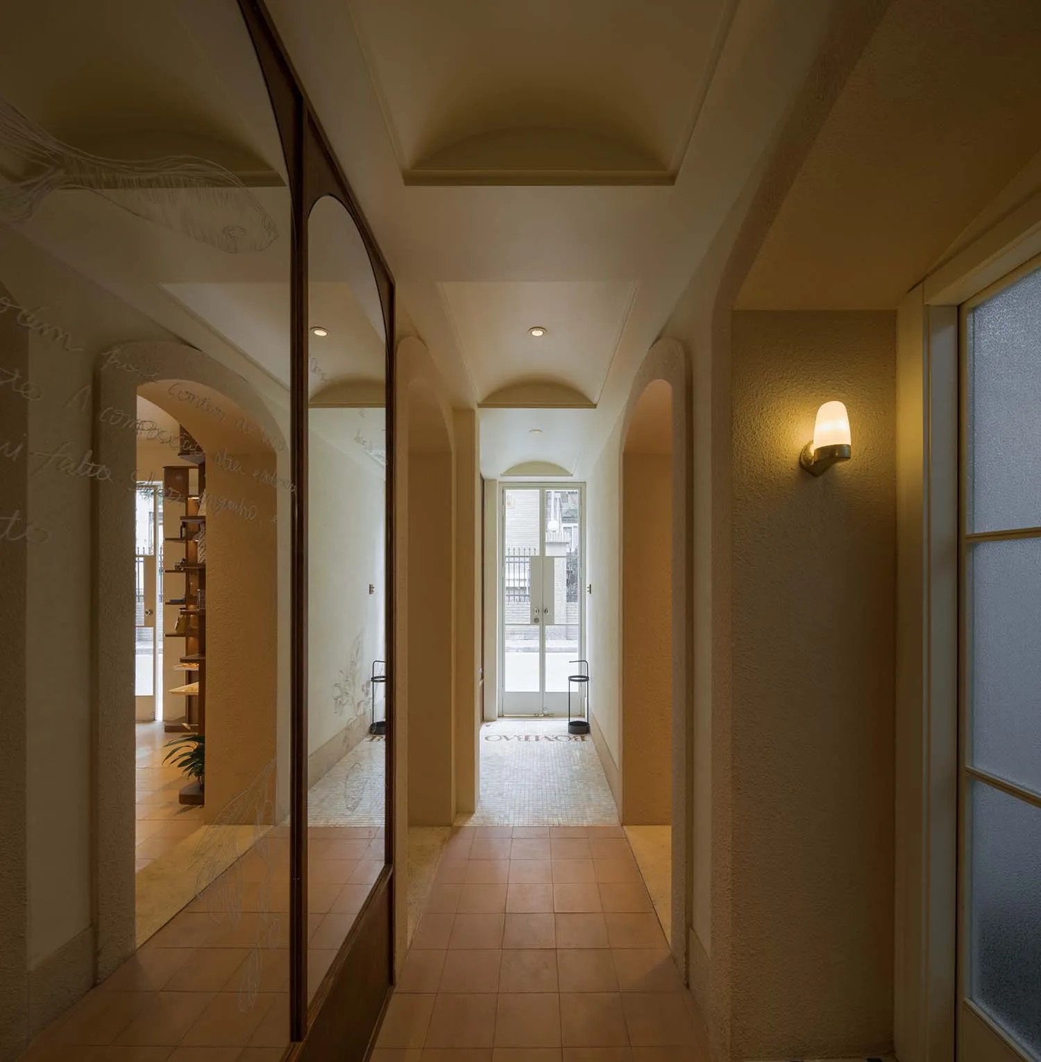 A modern hallway with a mirror and door, featuring a clean and modern look with tiled flooring and books placed along the space