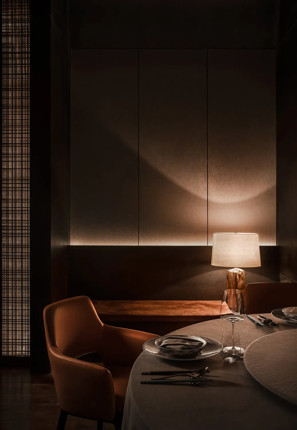 Dimly lit dining area with a table, chairs, and a smaller table in the background, featuring brown-toned walls and wine glasses