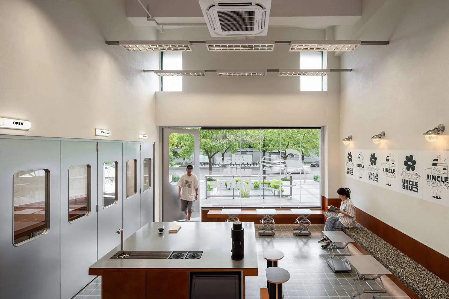 Modern lobby with a kitchenette, chairs, and a dining table, featuring a person sitting in one of the chairs