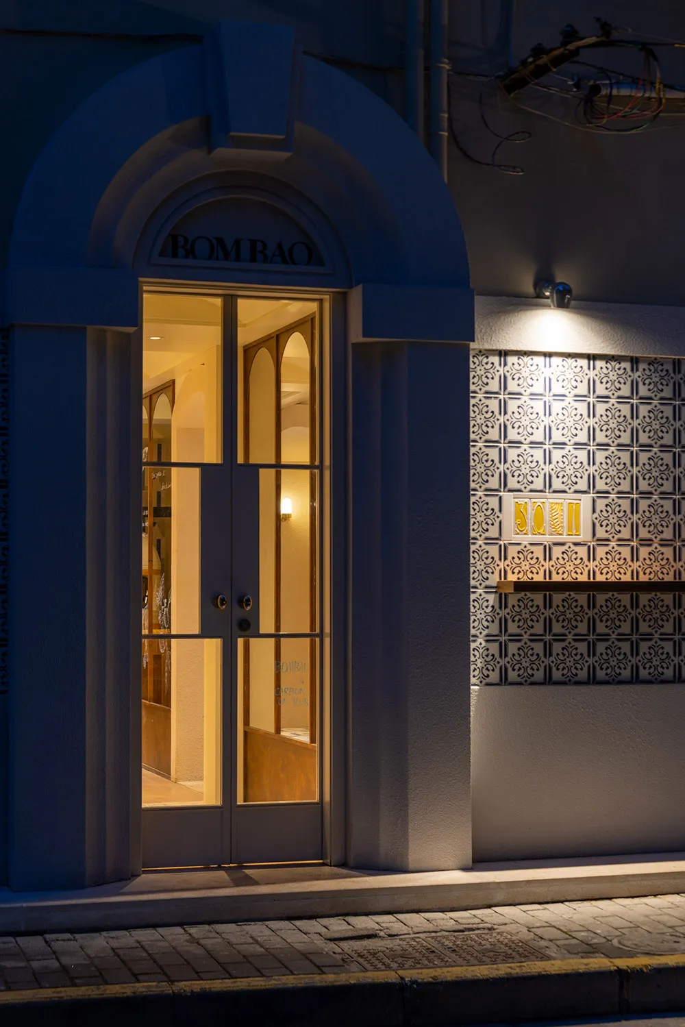A concrete building entrance with a decorative doorway featuring glass panels and illuminated by lights