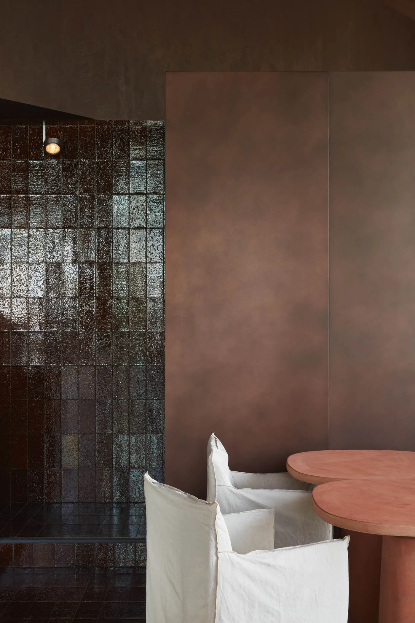 Cozy living space with a brown wall featuring a tile pattern, a dining table, and two chairs, one with a white cushion
