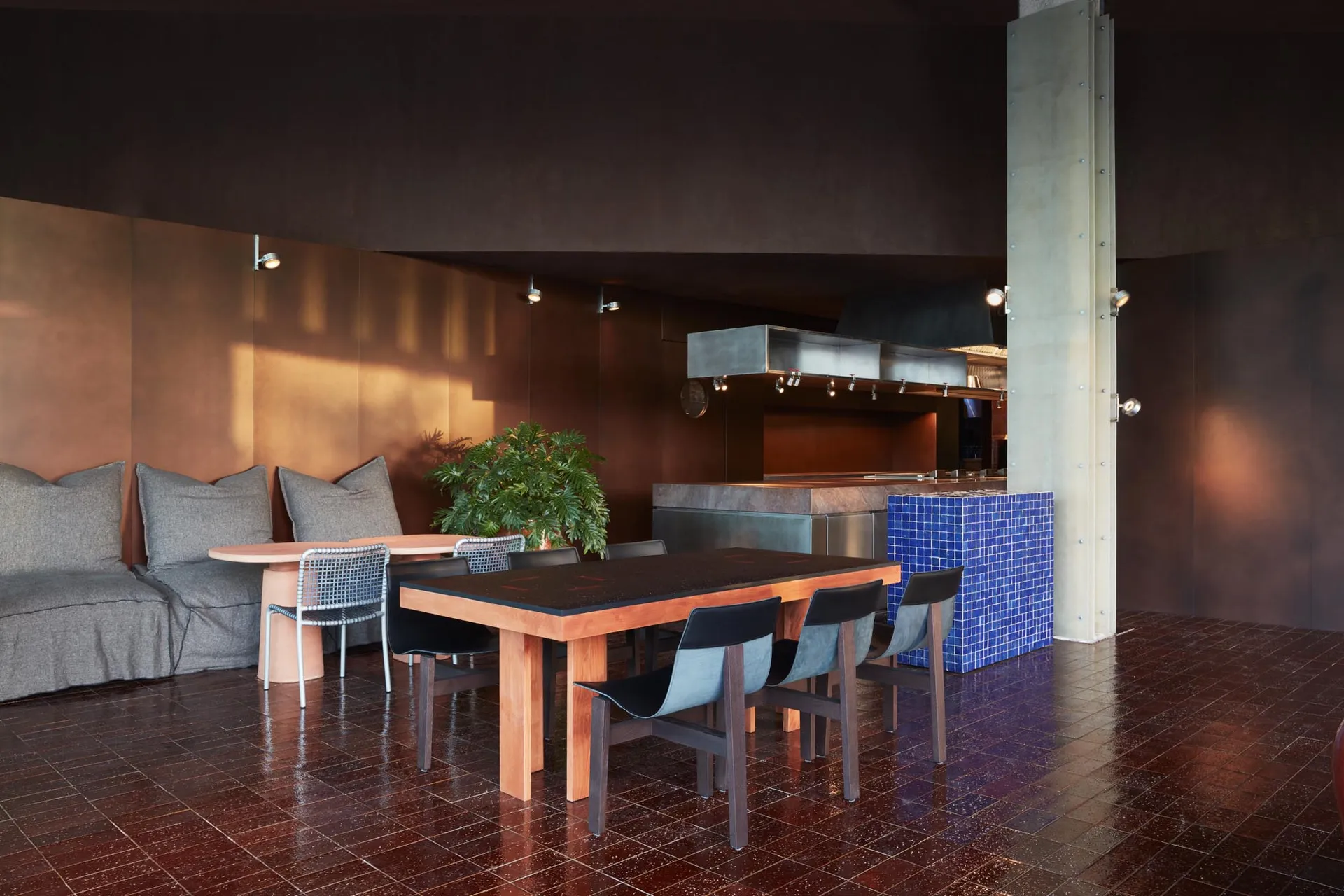 Modern kitchen dining space with a wooden table, black chairs, stainless steel appliances, and a potted plant