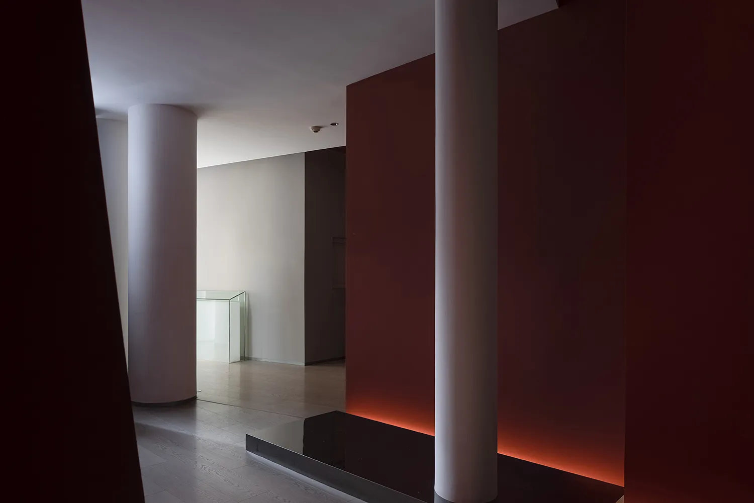 A calm and serene interior hallway with red walls, white columns, and a bench, giving a sense of grandeur