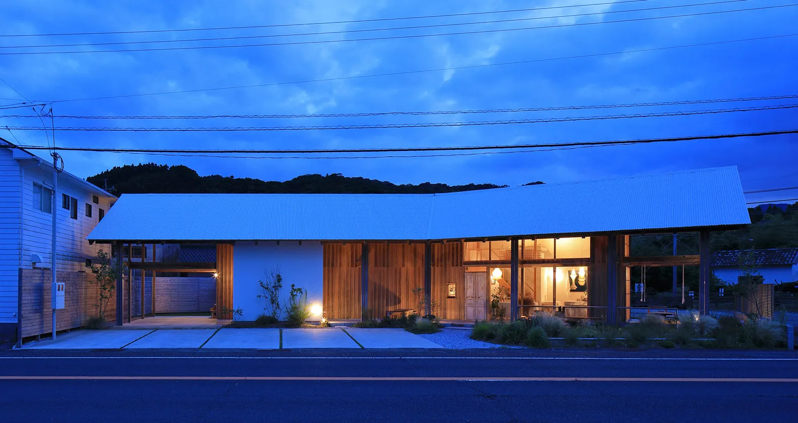 A well-lit white house with a wooden structure at night, surrounded by potted plants and two benches, conveying a sense of comfort and relaxation