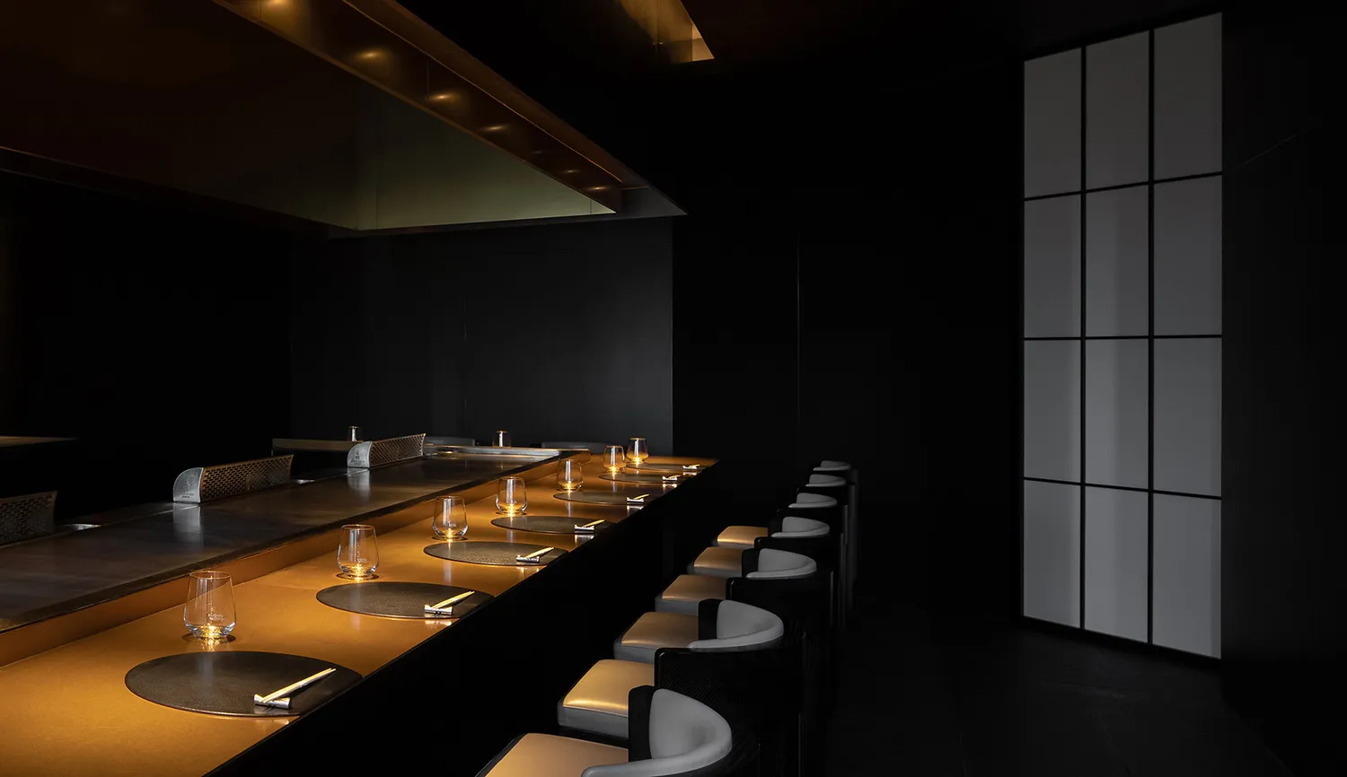 Dark restaurant kitchen with a black countertop and chairs, wine glasses, and an empty atmosphere