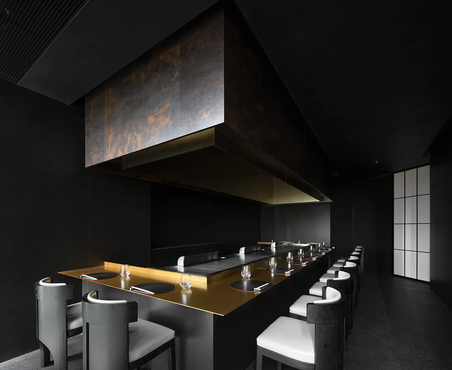Modern commercial kitchen with a large black countertop, dining table, and chairs, featuring various utensils and a hood for cooking