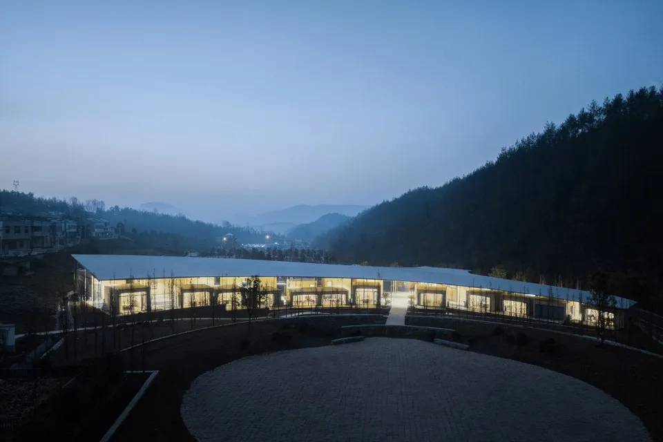 一座現代圓形建築，窗戶燈光亮起，襯托於黑暗背景