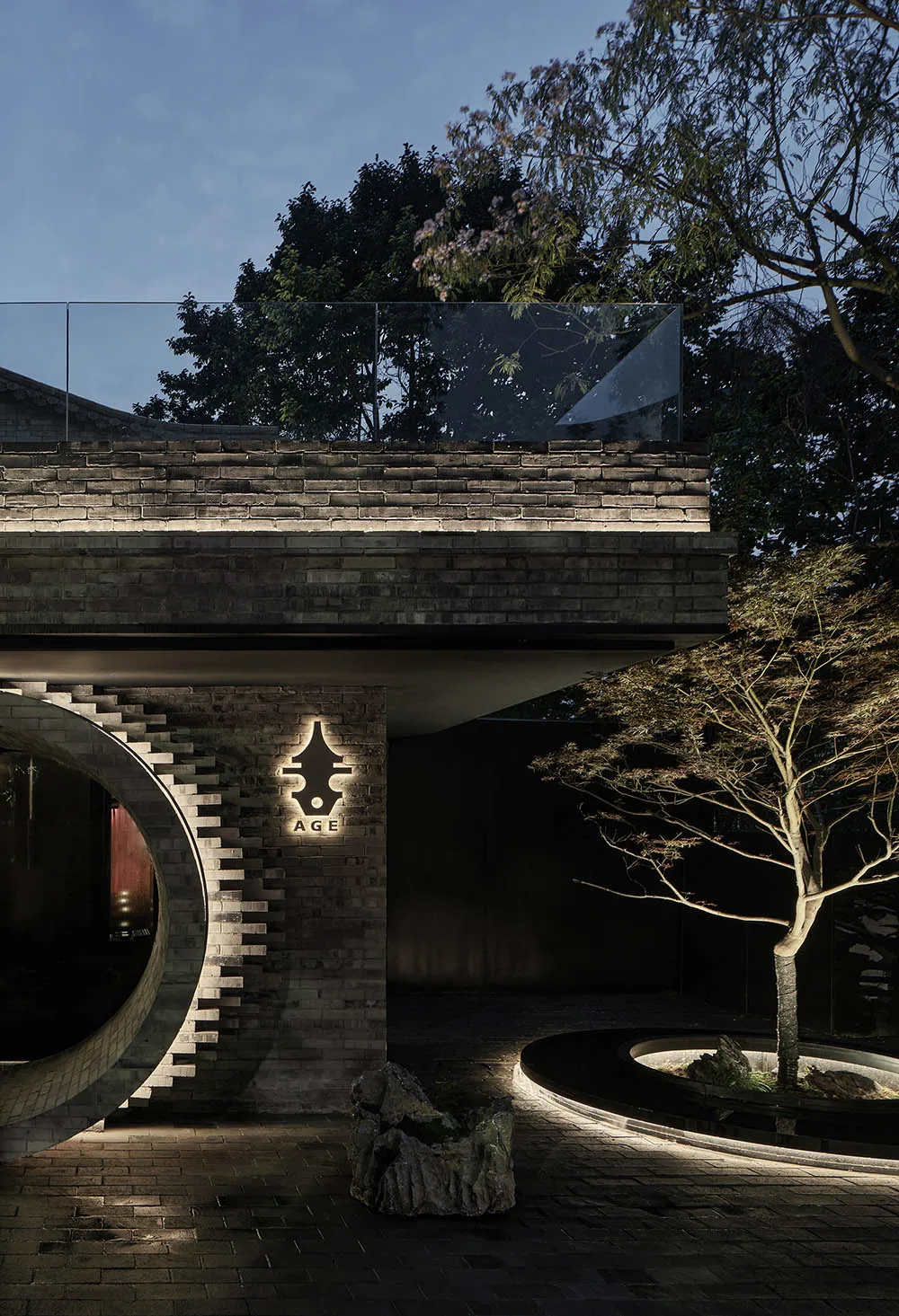 A modern building with a glass balcony featuring a brick design, surrounded by trees and a serene atmosphere