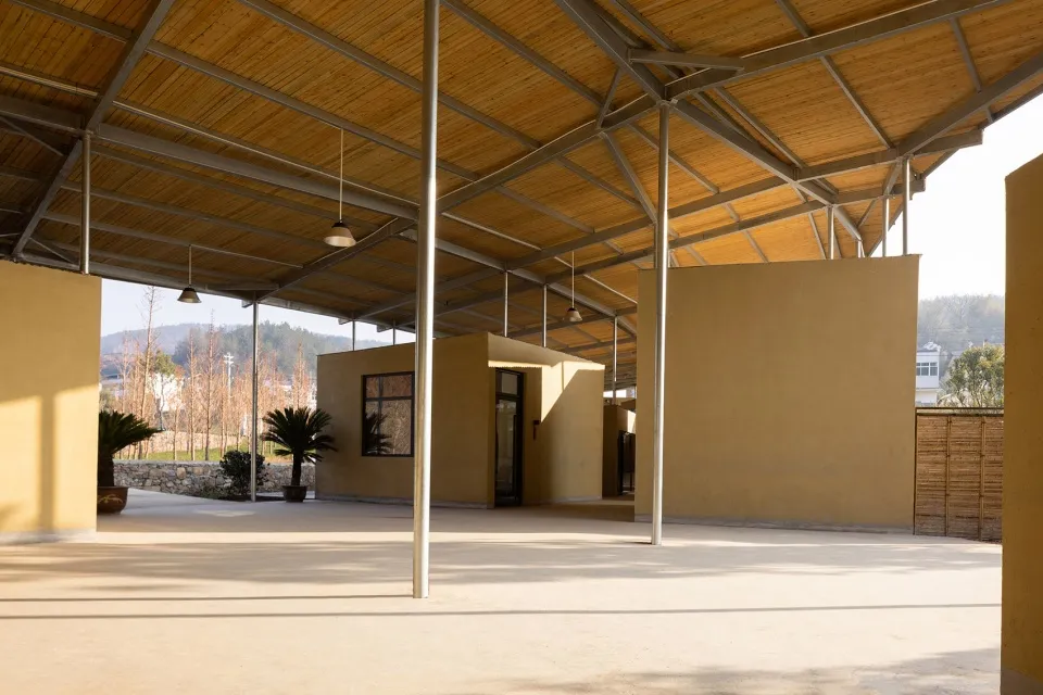 一座木造建築，配有木質屋頂，周圍環繞自然環境，建築附近有兩株盆栽