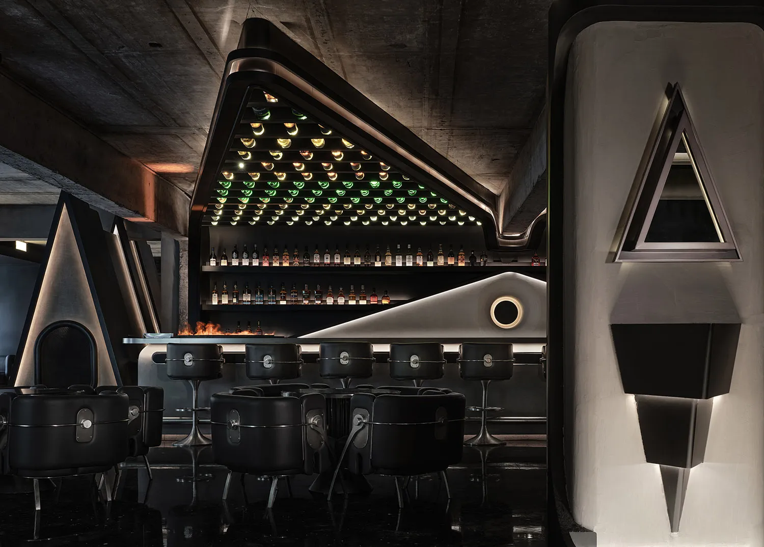 A dark and intimate bar area with a large number of bottles displayed on a wall, surrounded by comfortable seating and a bar