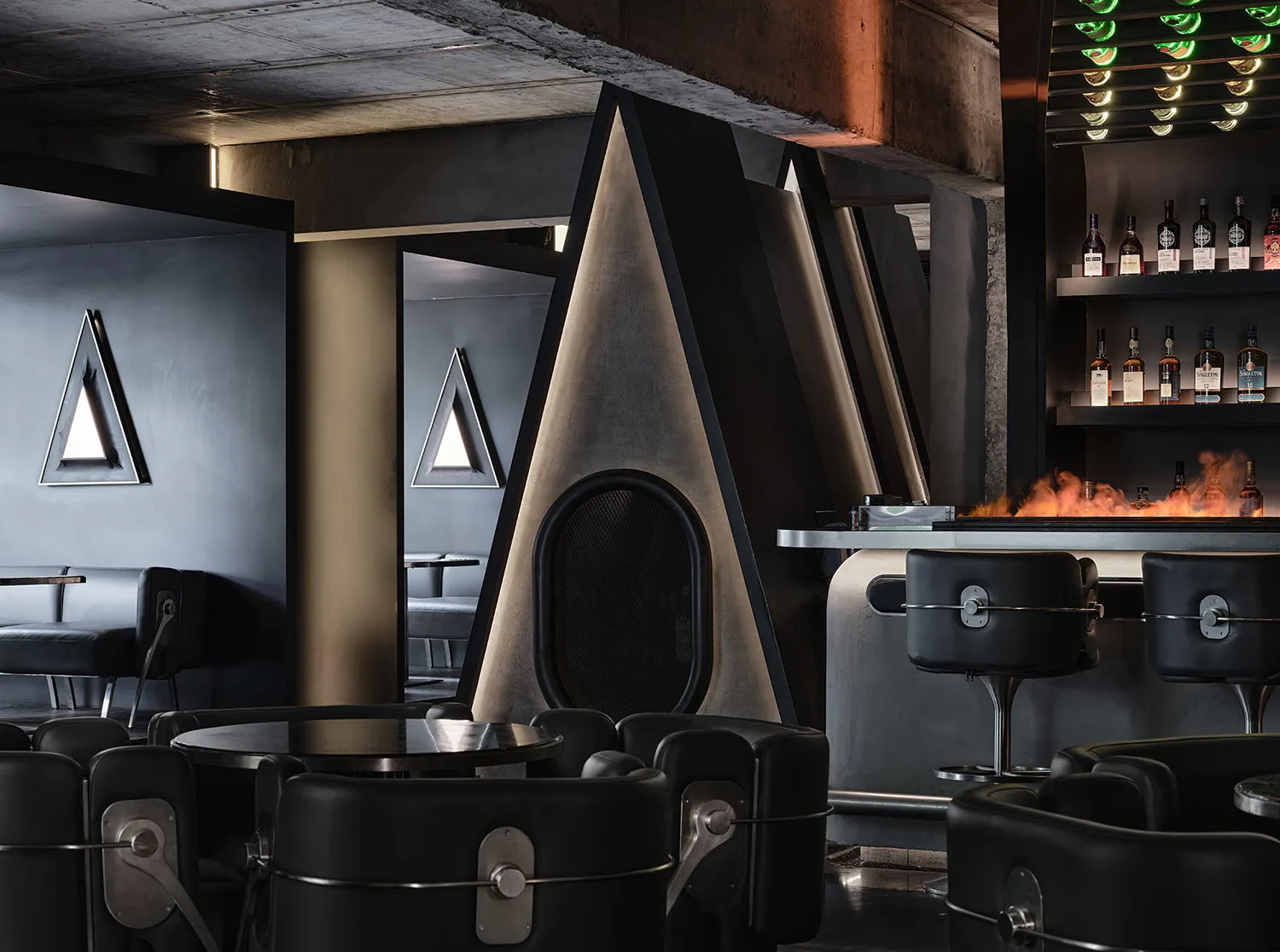 Modern bar area with a black leather lounge chair, dining table, and countertop with a sink, surrounded by bottles and featuring a stylish and comfortable atmosphere