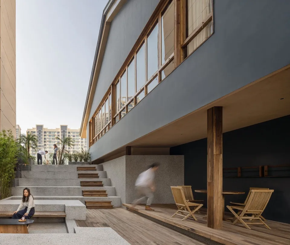 A rooftop gathering space with a glass facade, multiple levels, and people socializing in a lively atmosphere