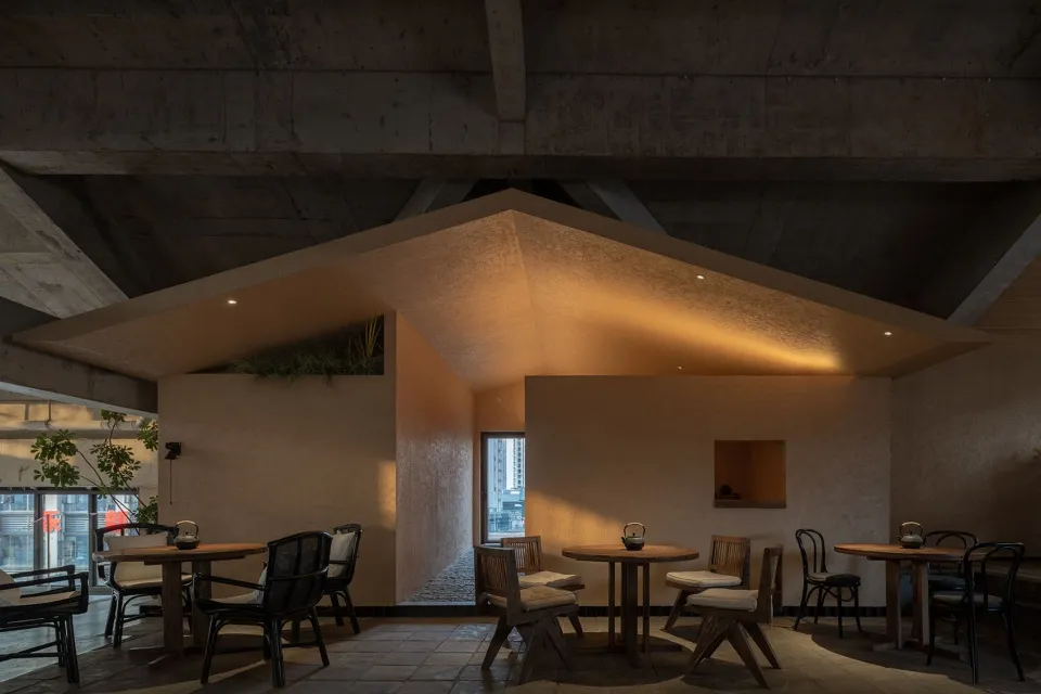 Industrial-style dining area with concrete walls, multiple tables, chairs, and lamps providing warm lighting
