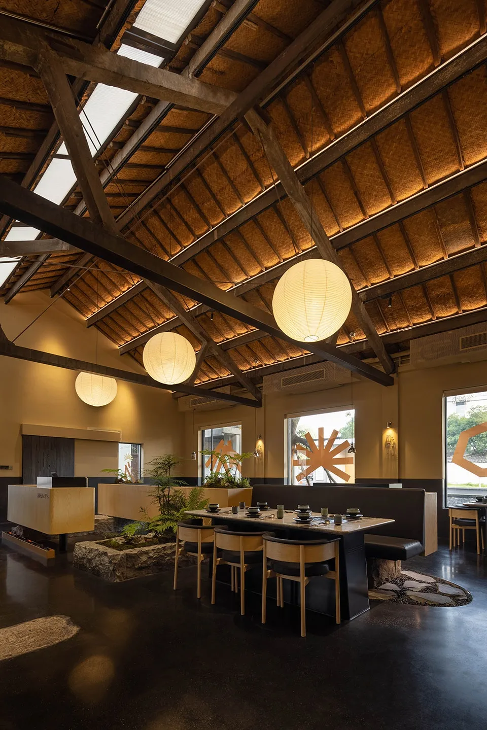 A modern restaurant dining area with tables, chairs, potted plants, hanging lights, and artwork on the walls