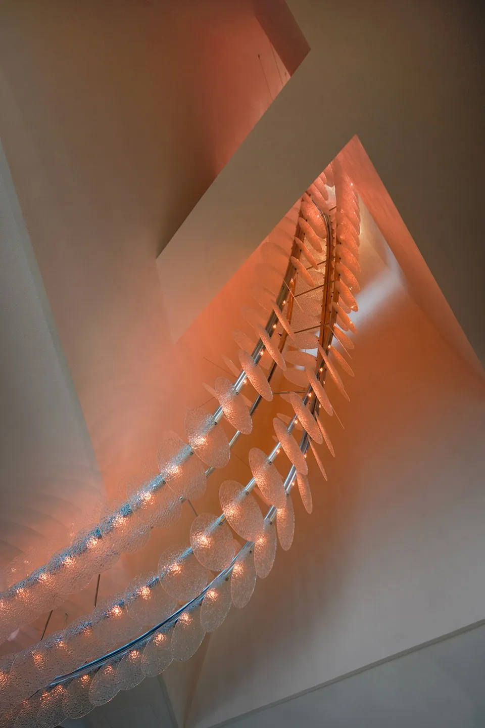 A modern stairwell with a glass chain link fence, illuminated by lights, creating a striking contrast between transparent and opaque elements