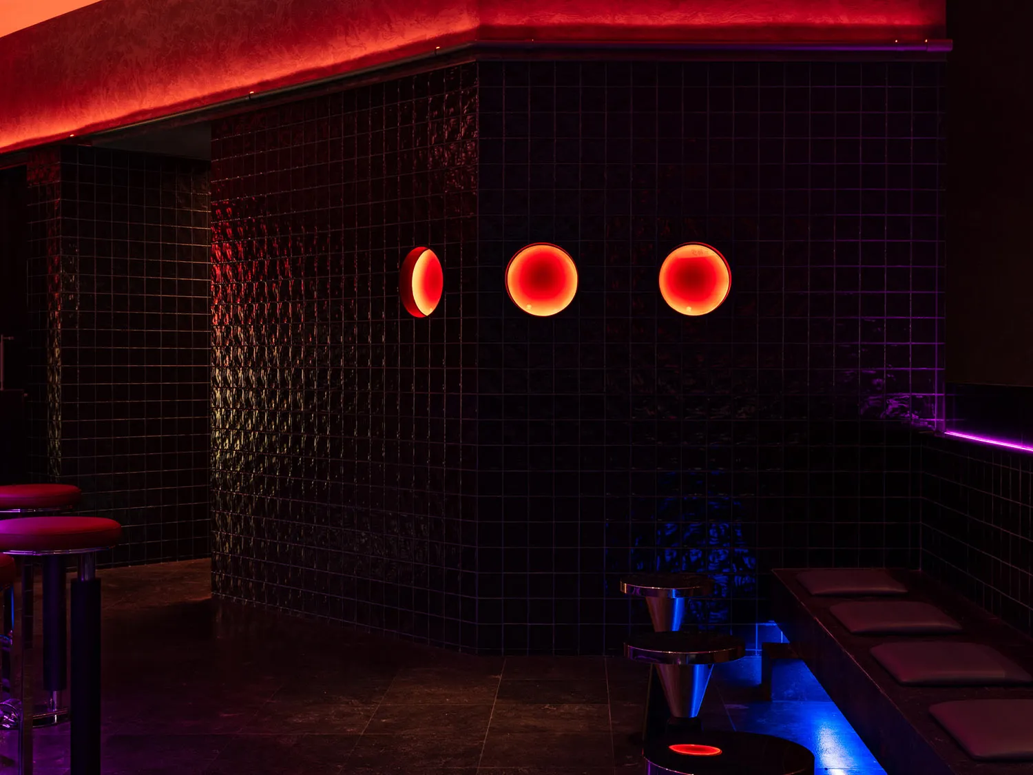 Bathroom with black walls, red accents, three round lights, a sink, and a bench, giving off a modern and sleek vibe