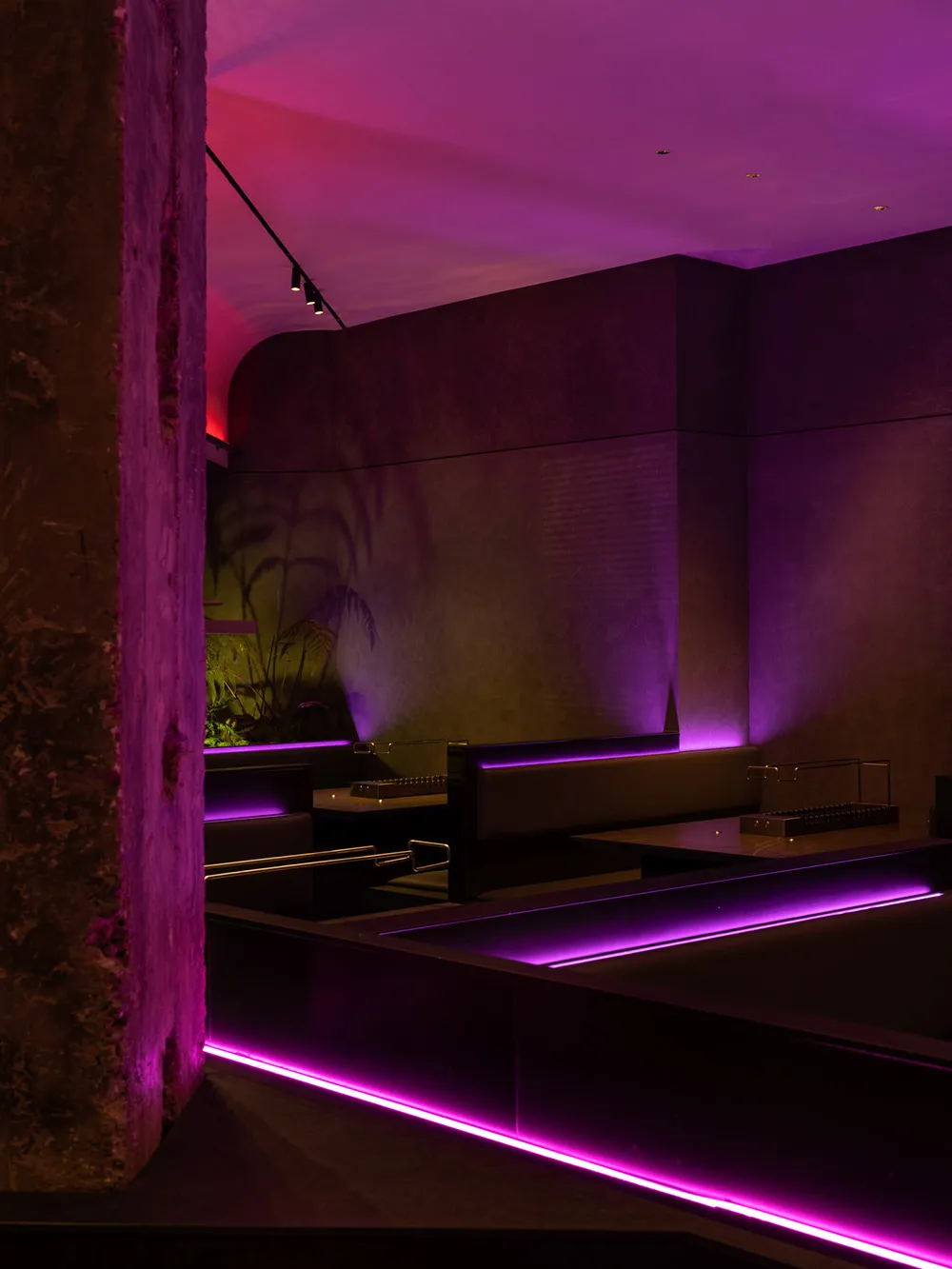 A modern restaurant with purple lighting, stone, and wood elements, featuring dining tables and chairs in a spacious and inviting atmosphere