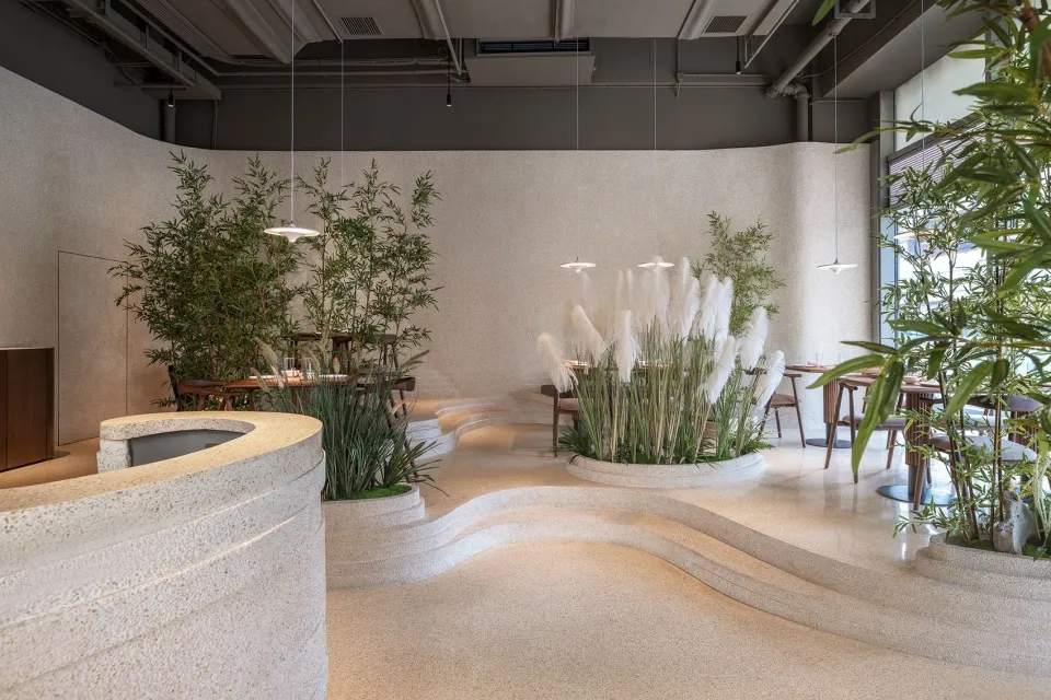 A restaurant interior with a large white wall, dining table, chairs, and potted plants, creating a comfortable atmosphere