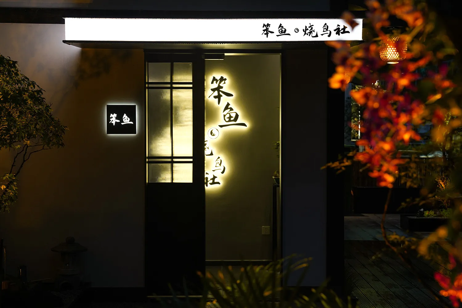 A calm and inviting Asian restaurant entrance with a wooden door, a sign indicating a bathroom, and two potted plants on either side