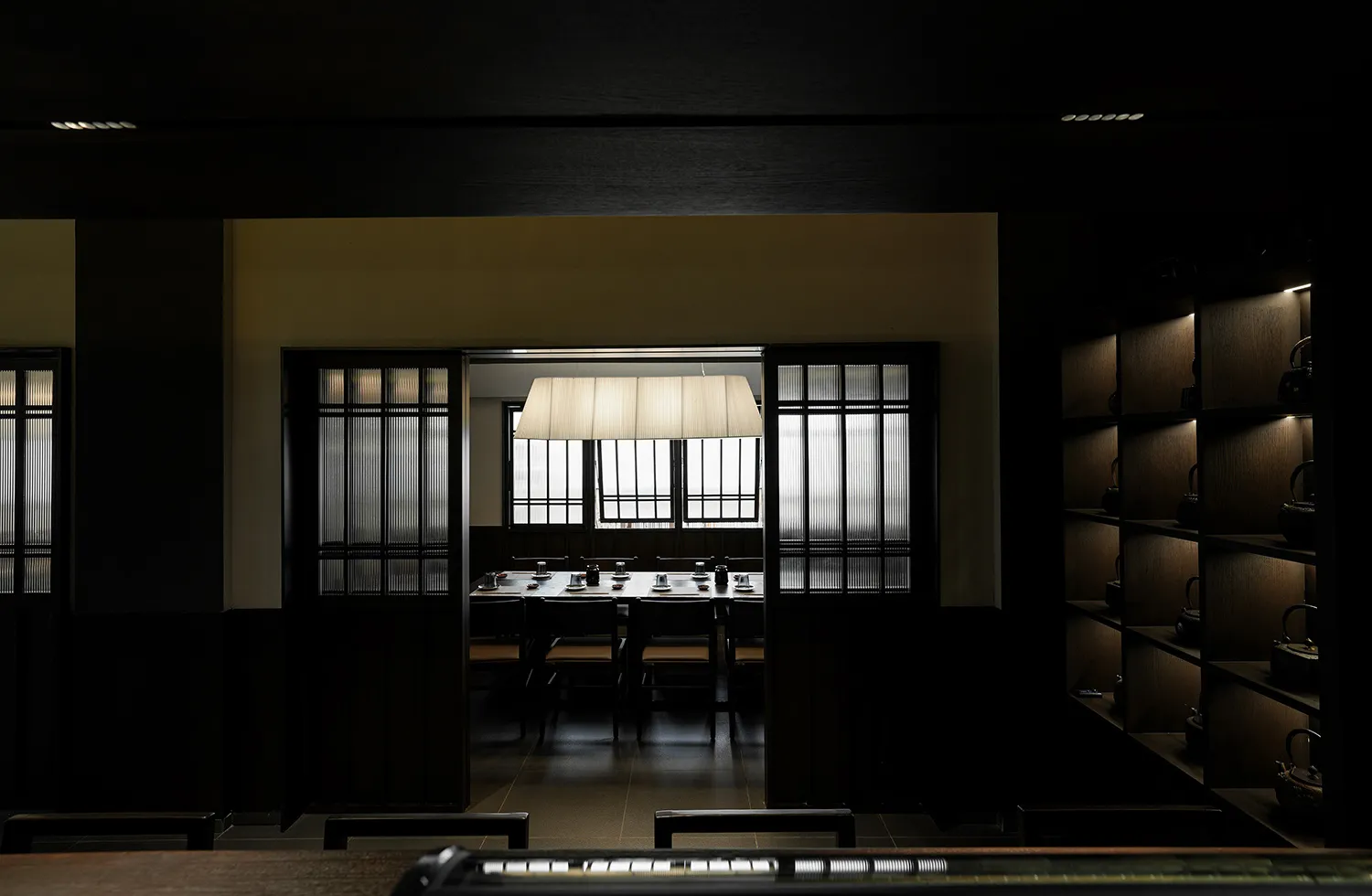 Dark dining space with wooden floors and walls, featuring chairs and tables arranged in a restaurant setting