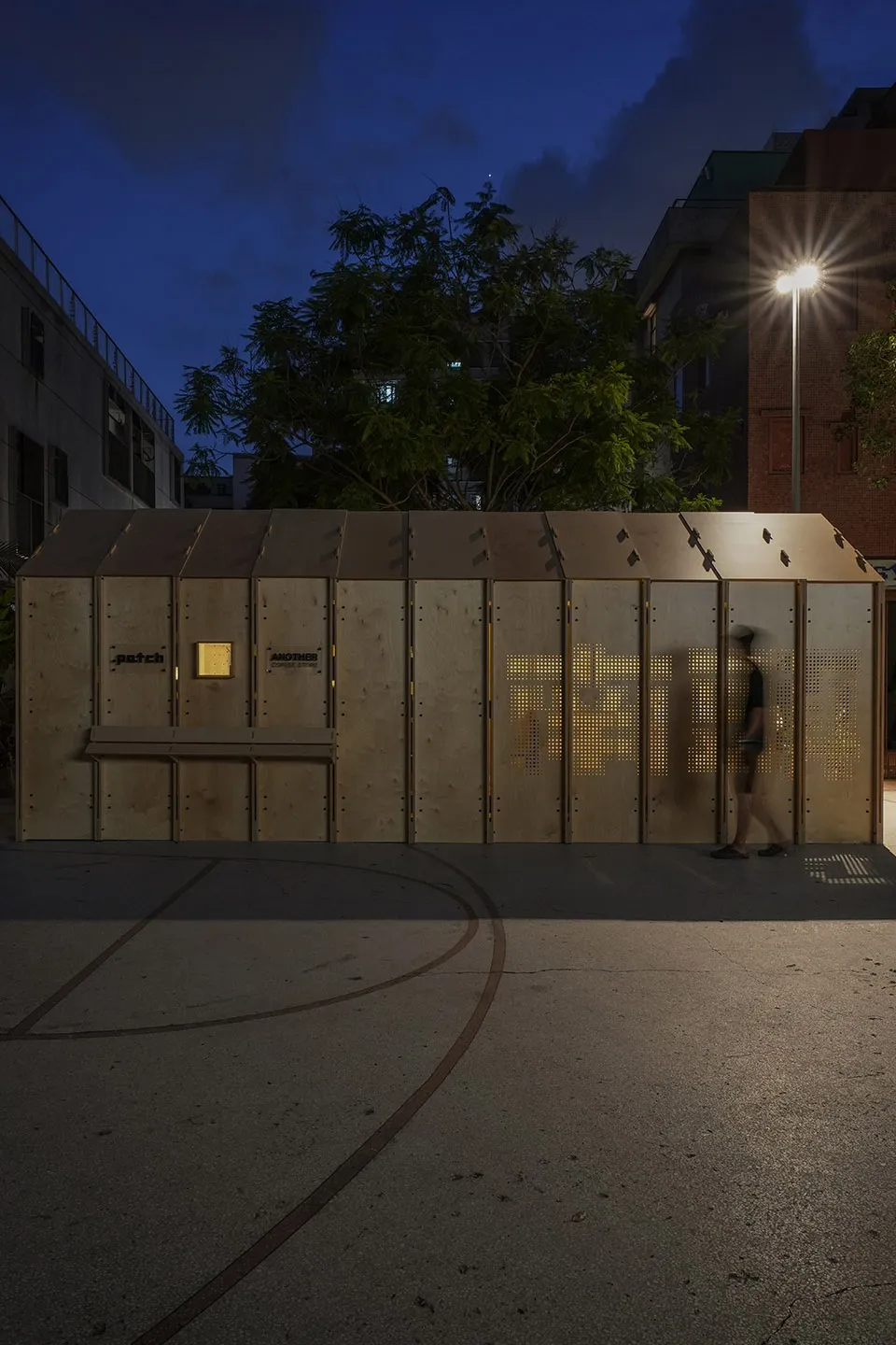 A wooden cabin with a bench outside the entrance, featuring two people standing near the building, conveying a sense of warmth and invitation