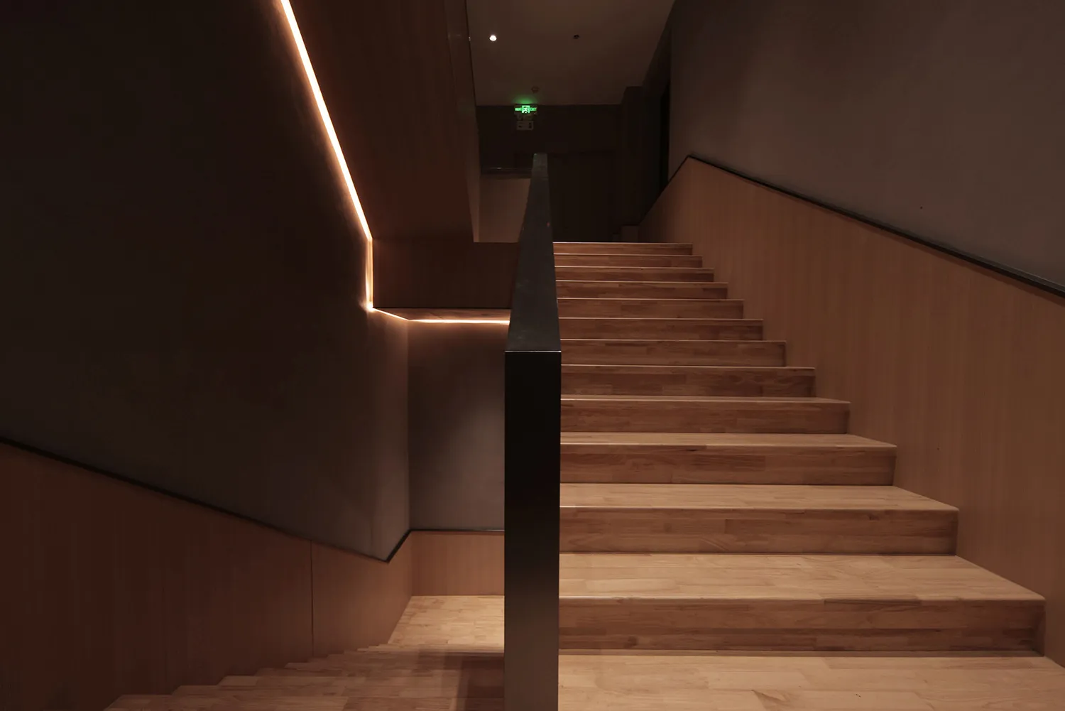 A photo of a staircase with a wooden structure, brown in color, and a black railing, set in a building with a sense of depth and dimension
