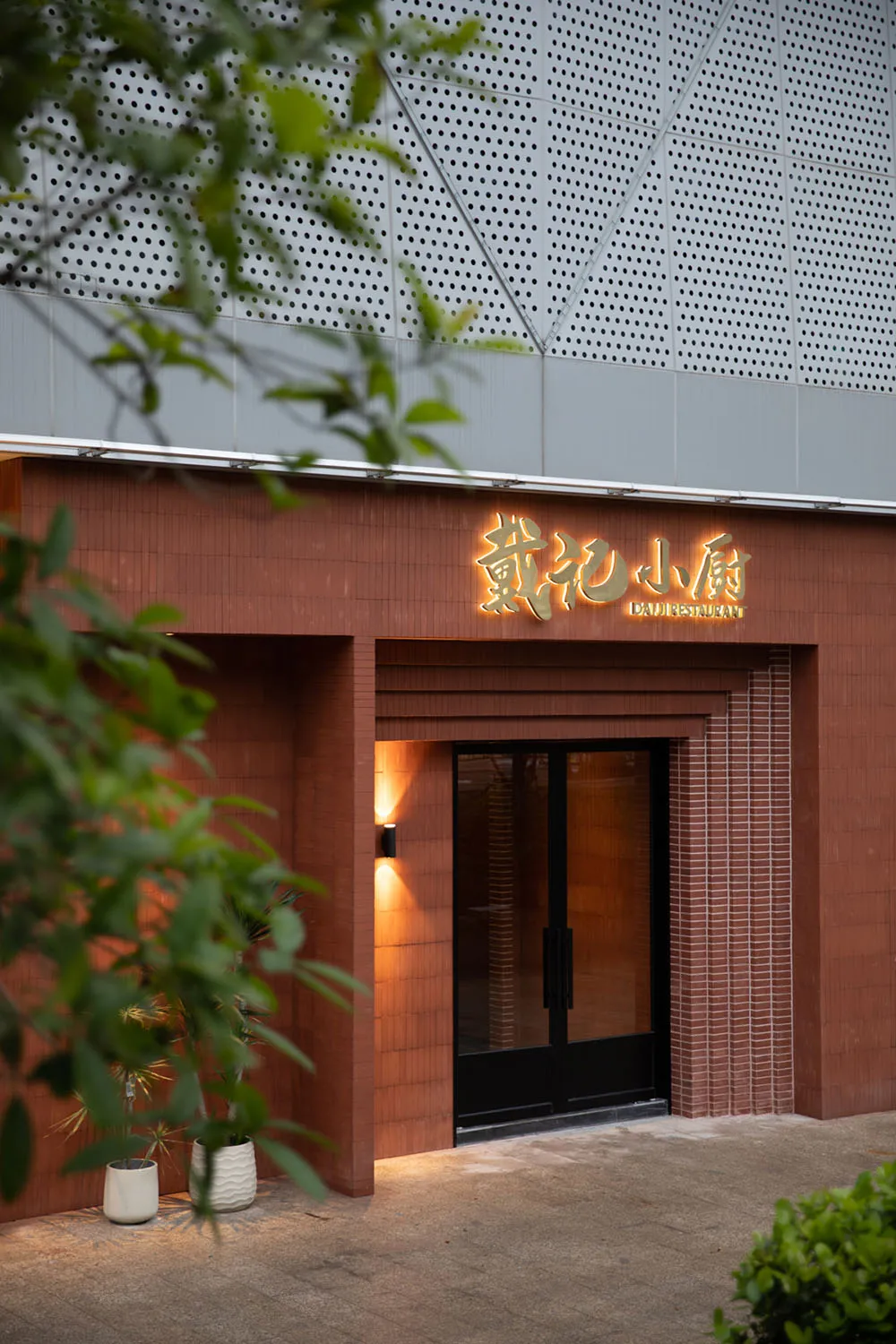 A welcoming Asian restaurant entrance with a wooden door, brick walls, and comfortable seating area