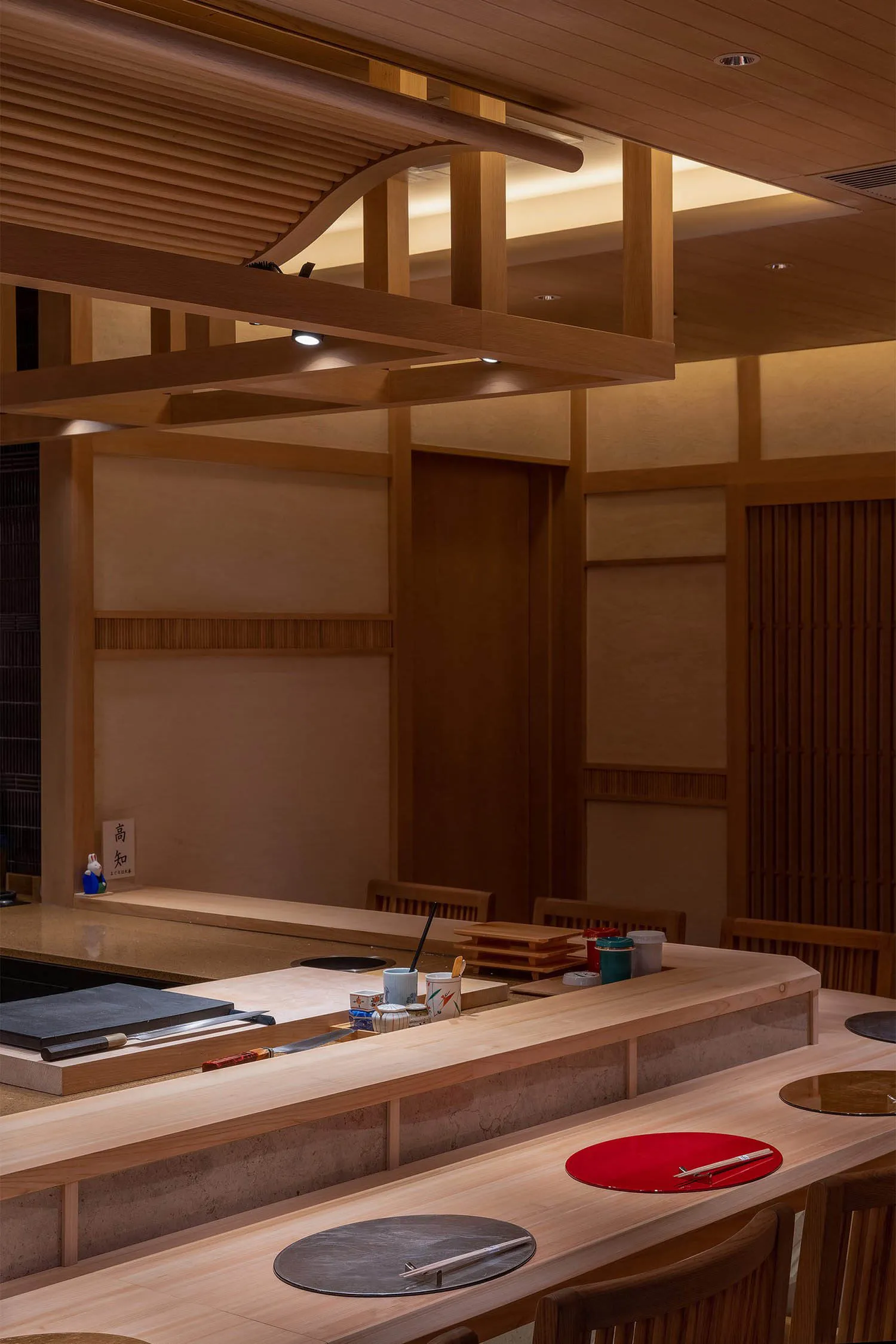 Warm and inviting Asian restaurant interior with wooden floors and walls, featuring chairs and tables with cups and a bowl