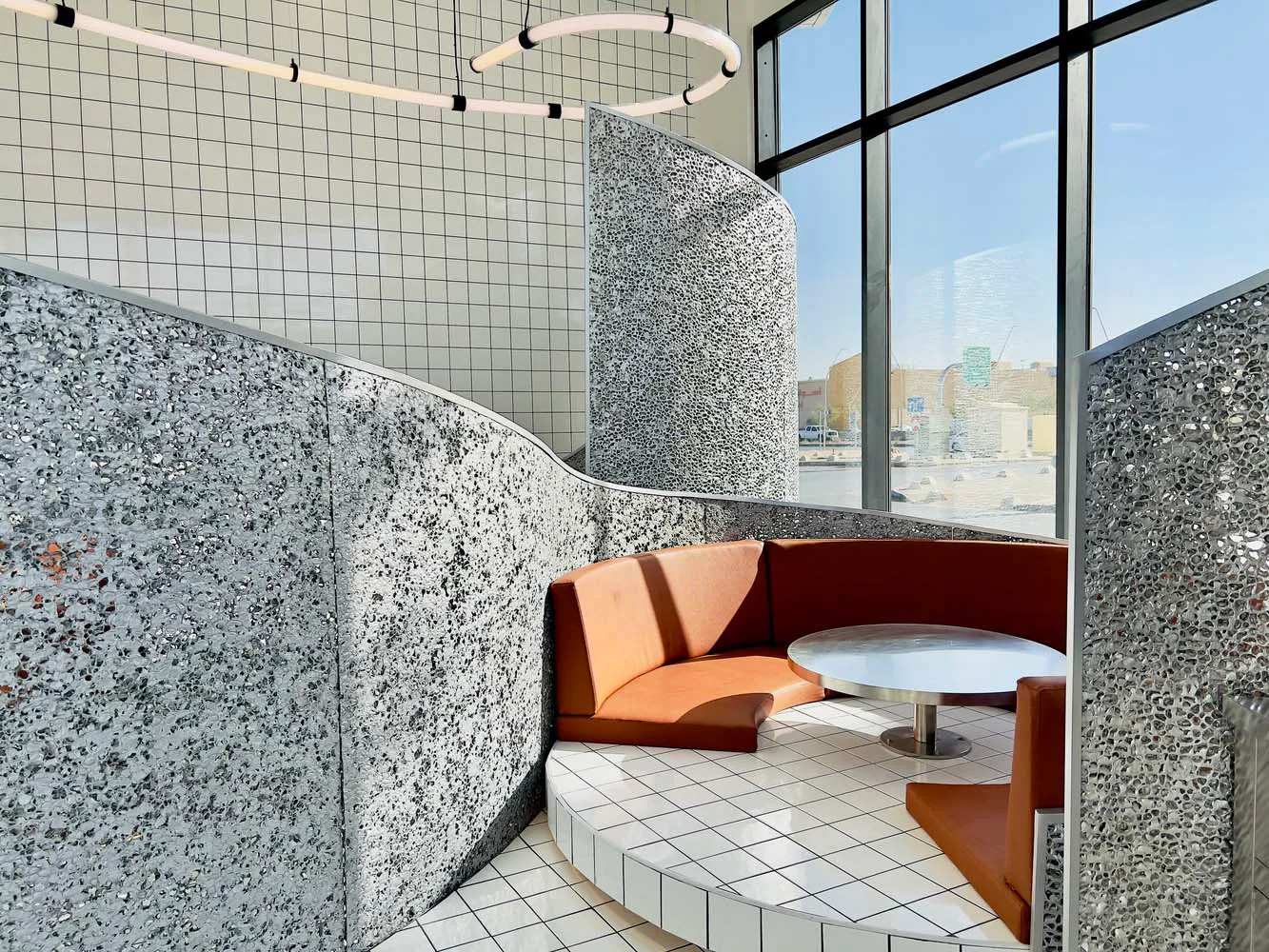 A modern restaurant with a circular dining area, stone-textured walls, and two seating areas, creating an inviting atmosphere for socializing and dining