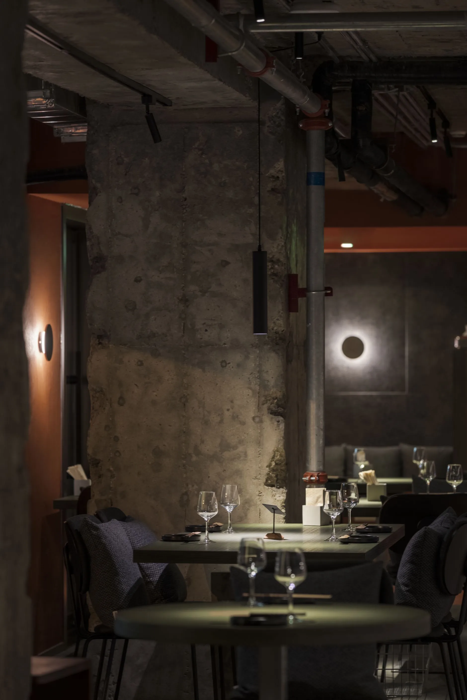 Dimly lit restaurant interior with a dining table, chairs, and wine glasses, surrounded by stone walls