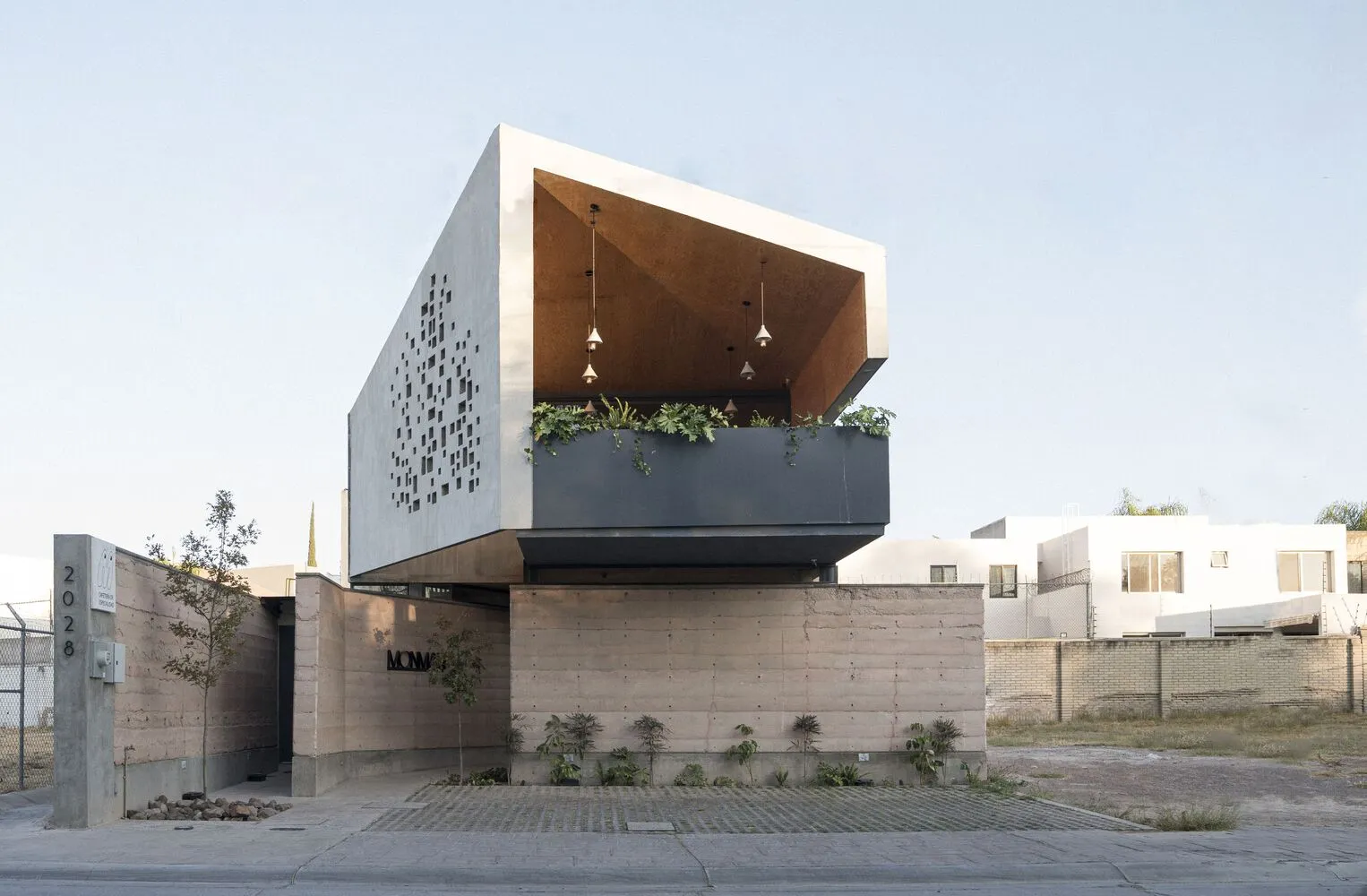 A modern building with a concrete facade, featuring a large overhang and potted plants around the structure, conveying a sense of urban design and contemporary architecture