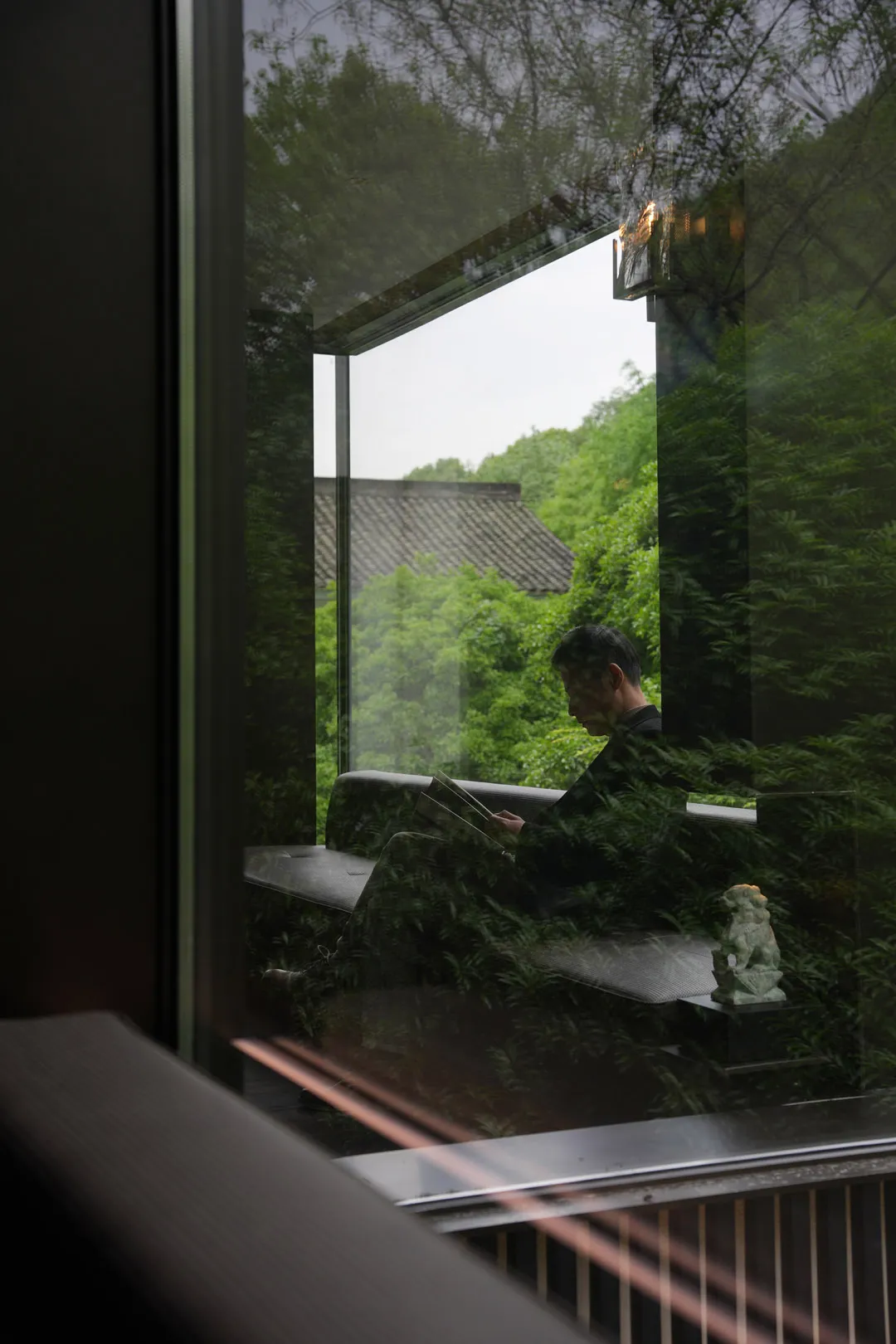 一名男子坐在寧靜客廳的長椅上，周圍環繞盆栽與窗外自然光線
