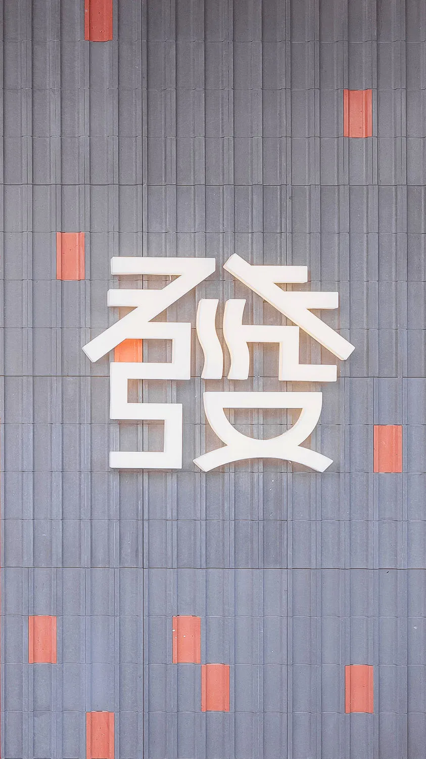 一座當代亞洲建築，擁有大型白色招牌，融入現代設計與橙色點綴，背後是都市景觀
