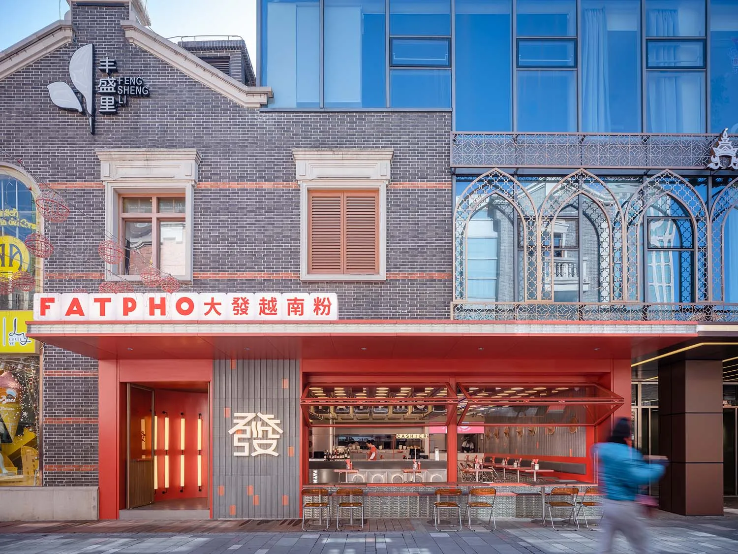 Lively Asian restaurant with red walls, orange trim, and multiple tables and chairs in a dining area with people seated and standing