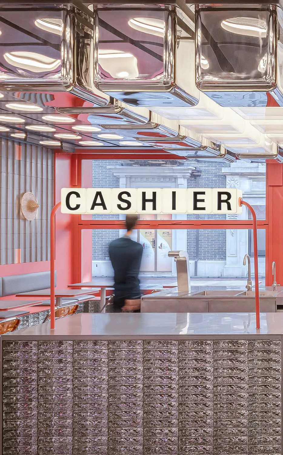 A casual restaurant cashier area with a counter, chairs, and a dining table, two people present