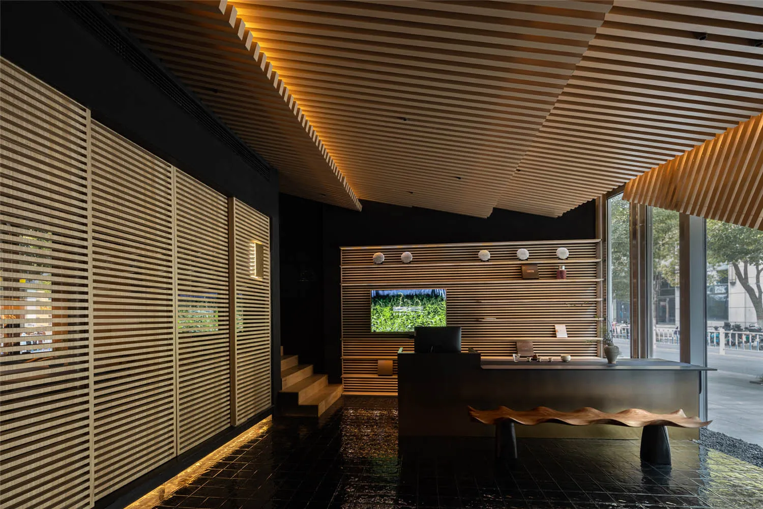 A hotel lobby with wooden walls and floors, featuring two mounted TVs, books, and a modern atmosphere