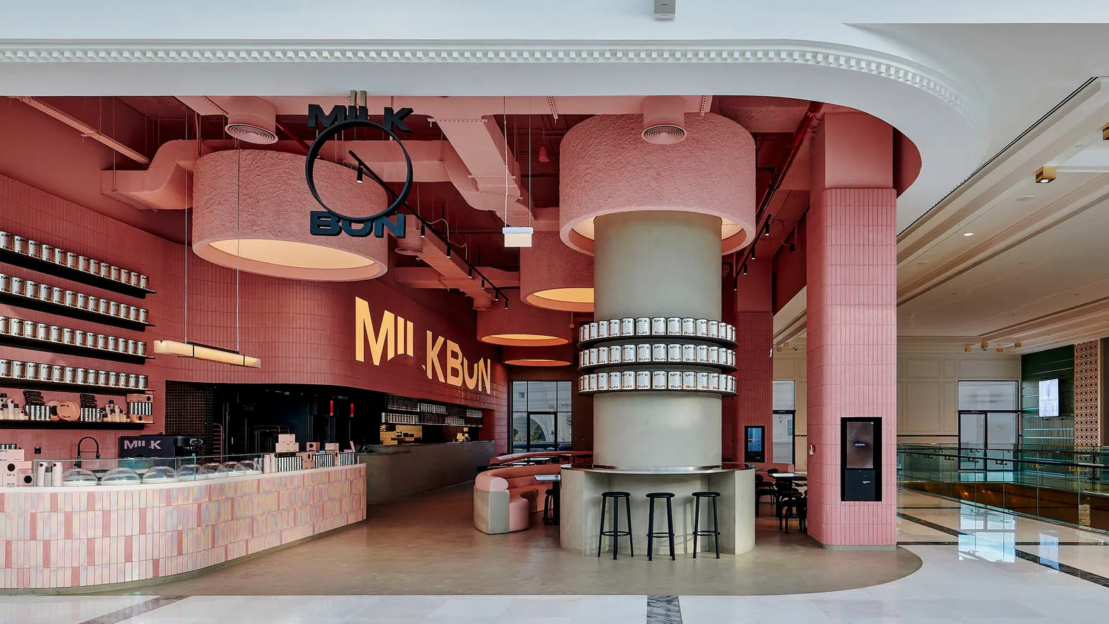 Inviting restaurant interior with a pink and white color scheme, featuring a bar, dining table, and various seating options, with bottles and a welcoming atmosphere
