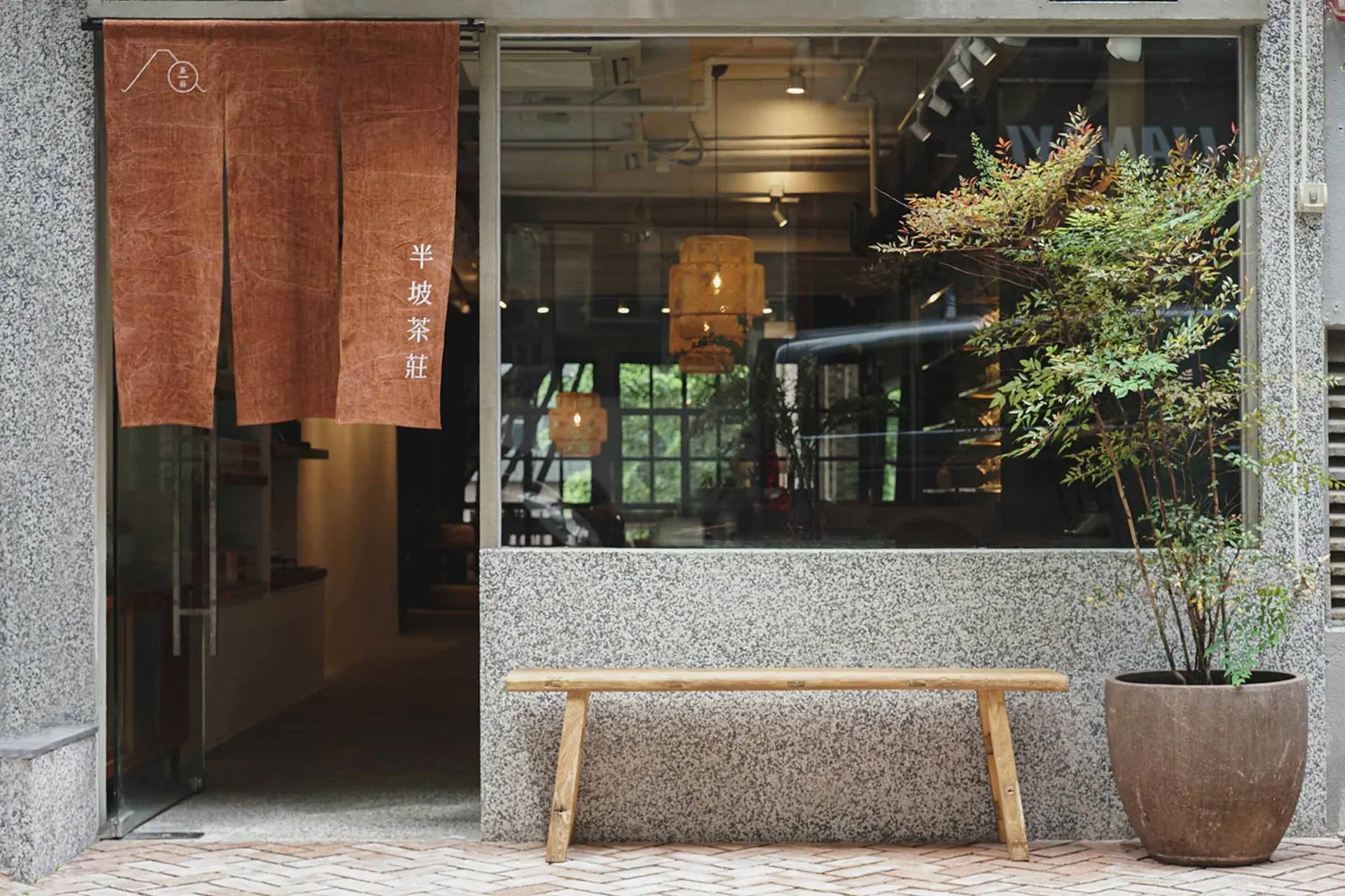 A well-lit Asian restaurant exterior with a wooden bench and potted plants, influenced by traditional Asian design elements